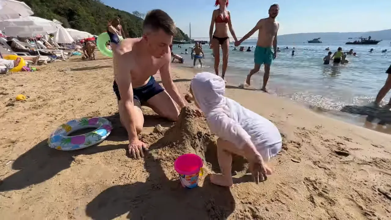 Family building a sandcastle on a sandy beach with swimmers and boats in the distance