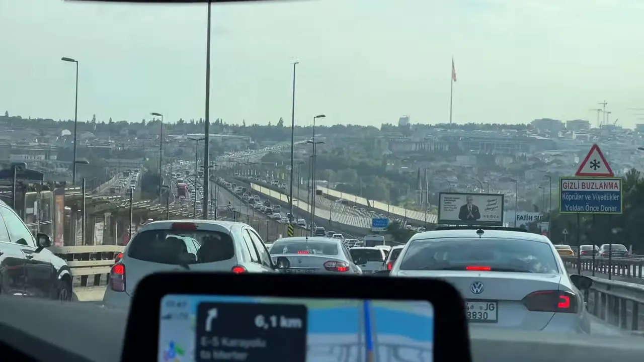 Heavy traffic stretching along an Istanbul highway and bridge, seen from inside a car with a navigation screen in the foreground.