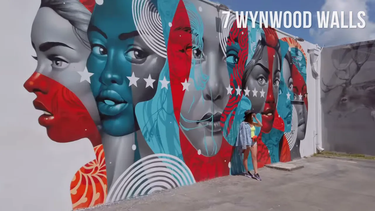 Vibrant multi-colored mural of overlapping female faces at Wynwood Walls with a visitor standing nearby