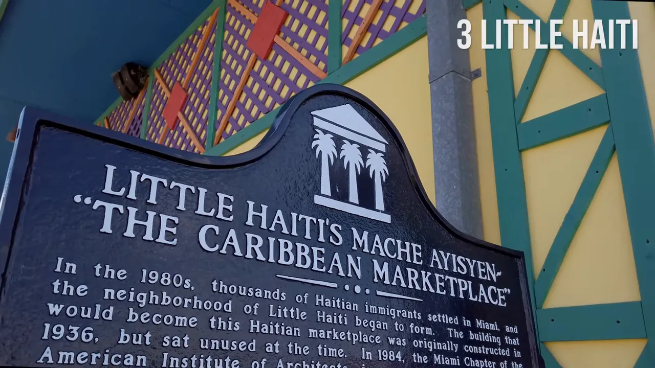 Plaque reading 'Little Haiti's Mache Ayisyen - The Caribbean Marketplace' mounted on a colorful facade
