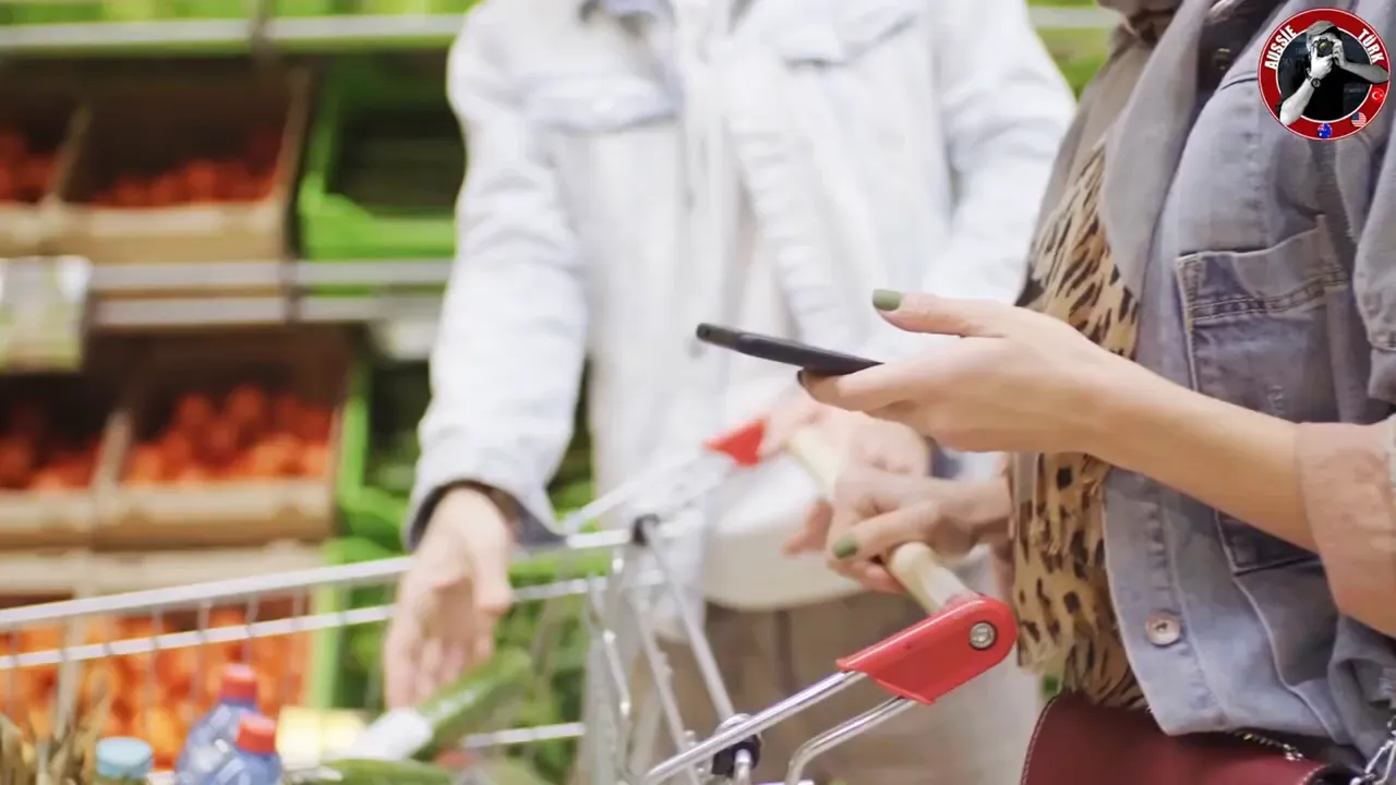 Alışveriş arabası, elde telefon tutan kişi ve market reyonlarına yakın plan.