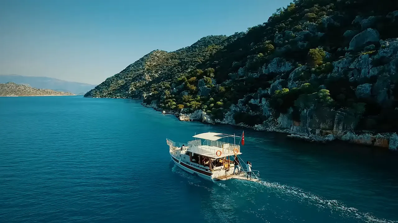 small charter boat cruising along clear turquoise waters beside steep, pine‑covered cliffs