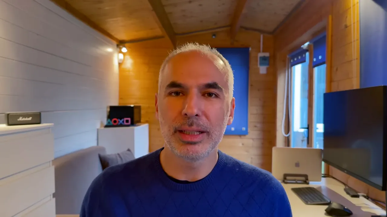 Konuşmacı merkezde, ev ofisinde kamera karşısında konuşuyor; masa, diz&uuml;st&uuml; ve monit&ouml;r arka planda