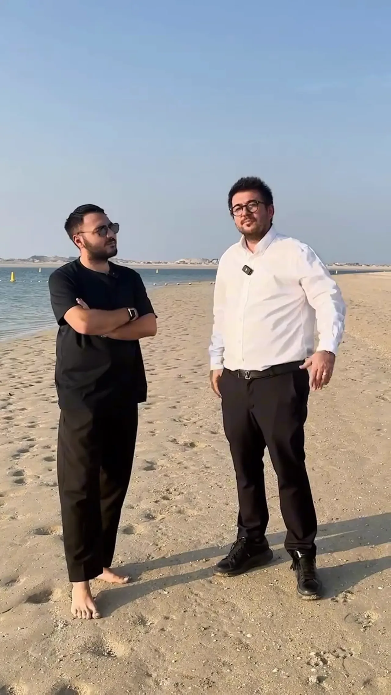 İki kişi Dubai Island plajında duruyor, arka planda sakin deniz ve kumsal g&ouml;r&uuml;n&uuml;yor.