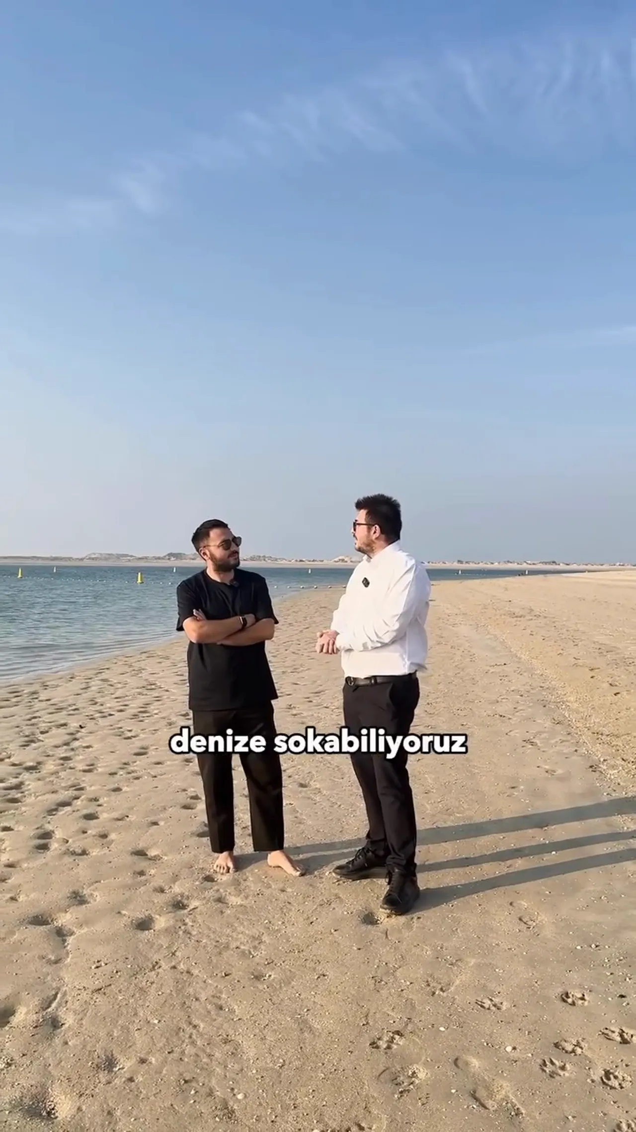 İki kişi Dubai Island sahilinde konuşuyor; kumsal ve deniz net şekilde g&ouml;r&uuml;n&uuml;yor.