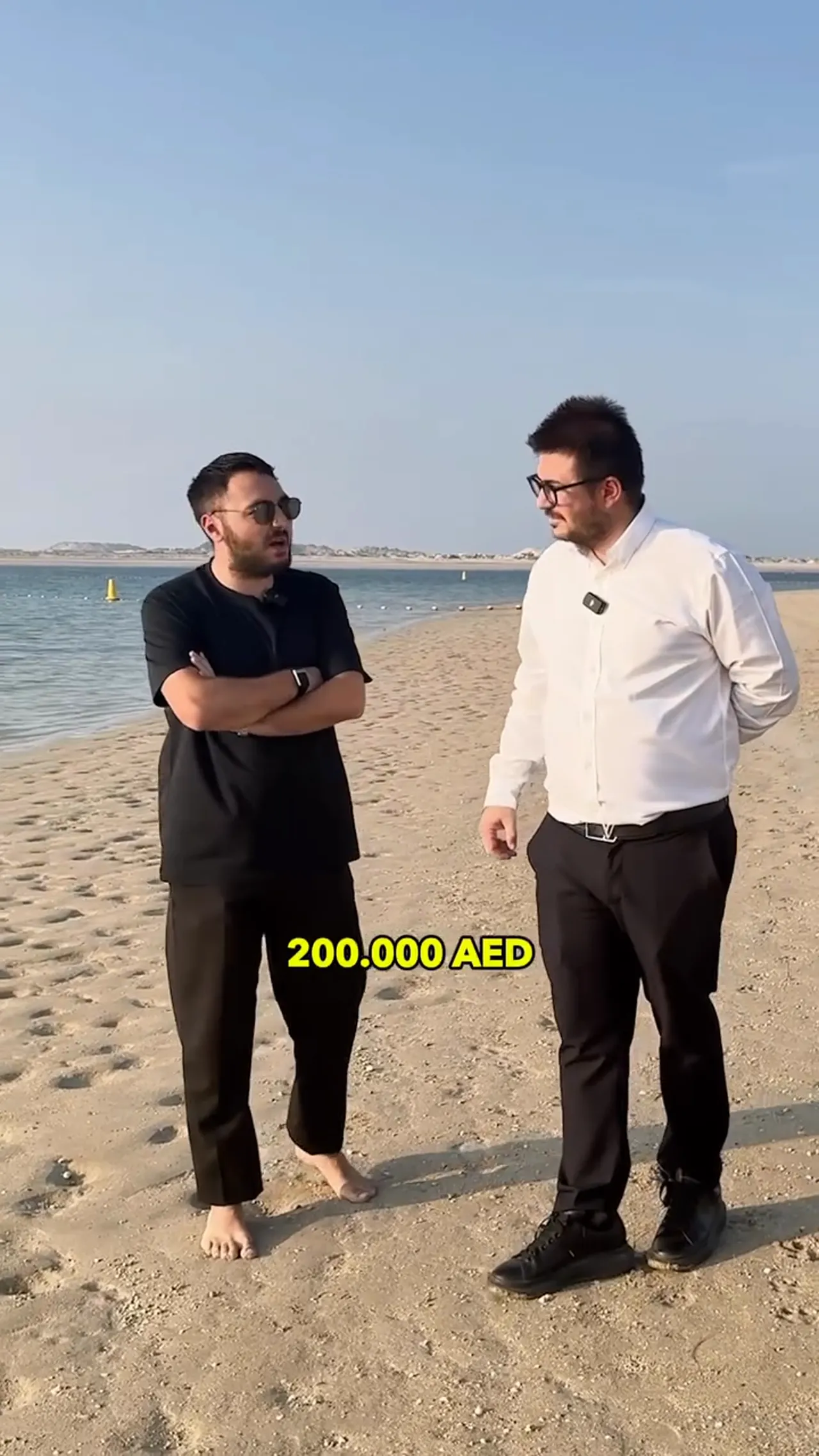 Plaj kenarında konuşan iki kişi; ekranda b&uuml;y&uuml;k sarı yazıyla '200.000 AED'.