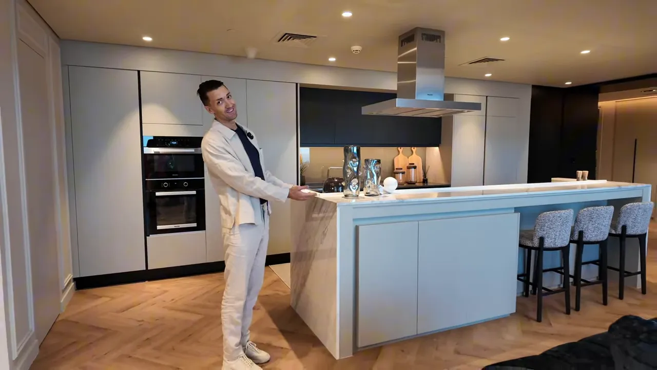 Wide shot of a finished modern kitchen with an island and a presenter pointing out features.