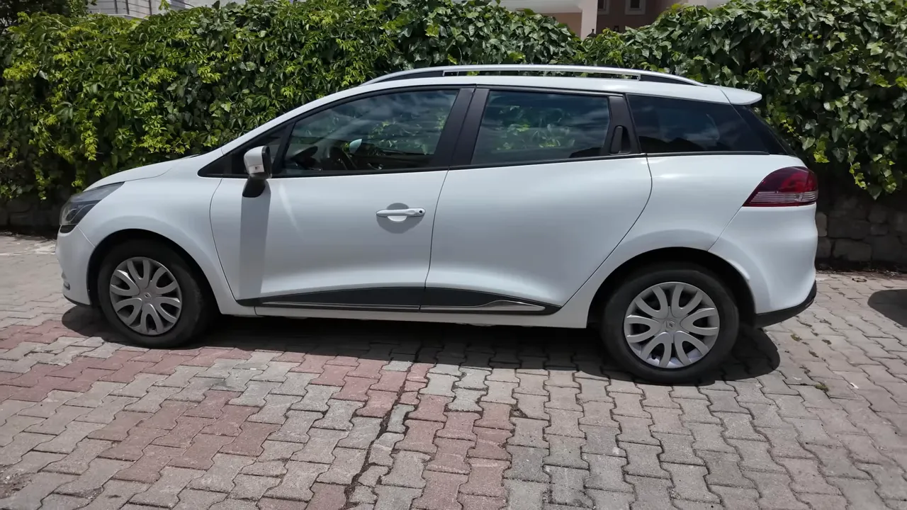 white compact car parked on a paved driveway in front of residential greenery