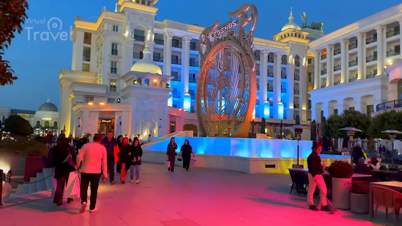 Grand hotel facade with large decorative sculpture and colorful plaza lighting at dusk