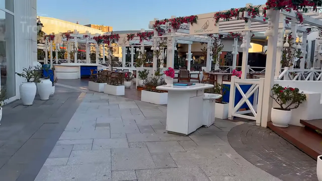 Empty promenade with white pergolas, planters and outdoor dining tables in daylight