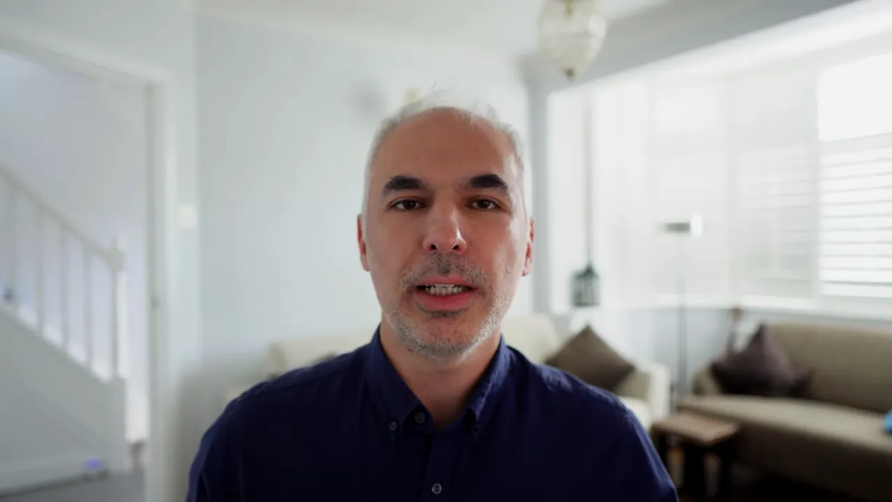 Sunucu ev ofisinde kameraya bakıyor; net, merkezde kadrajlanmış bir portre.