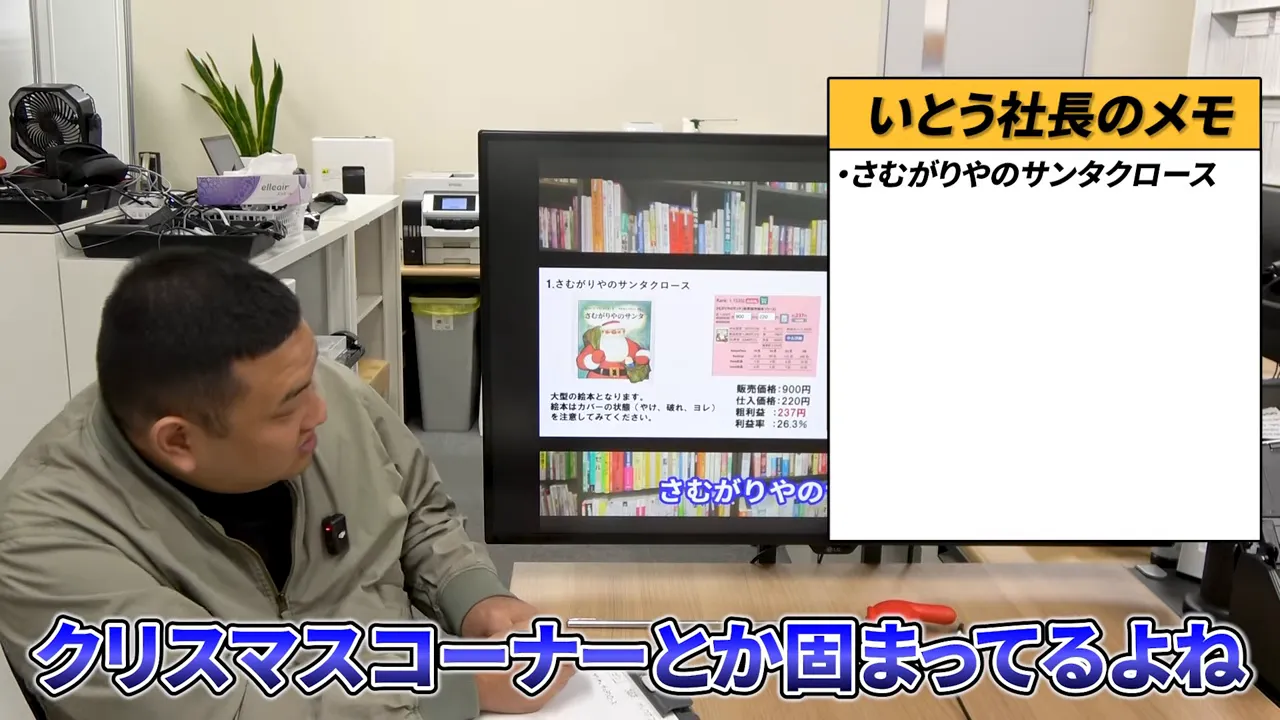 オフィスのテーブル越しにテレビモニターと話す男性、字幕に「クリスマスコーナー」と表示されたスクリーンショット