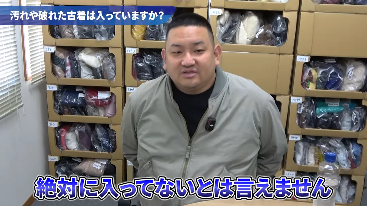 段ボール棚に梱包された古着を背に座って説明する人物と、上部に質問バナーがある映像の一コマ
