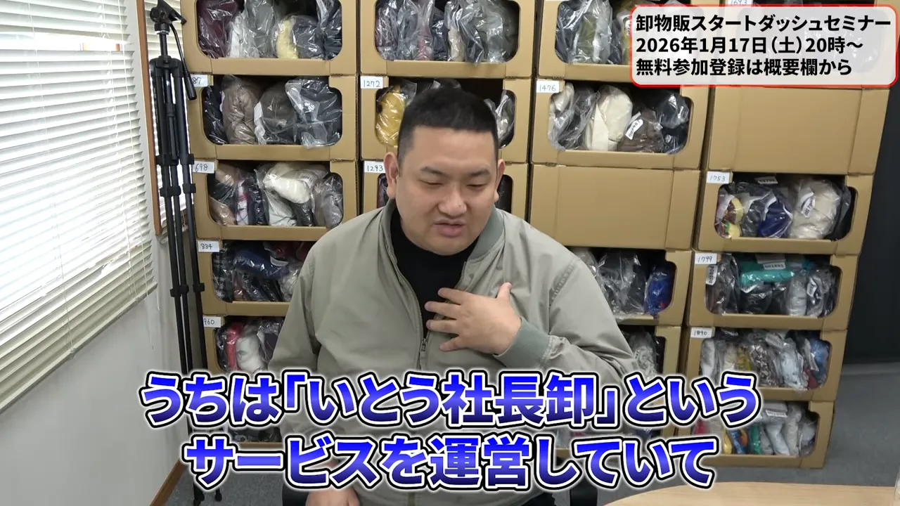 段ボール棚を背景に座りながら胸に手をあてて話す講師のクリアな正面カット