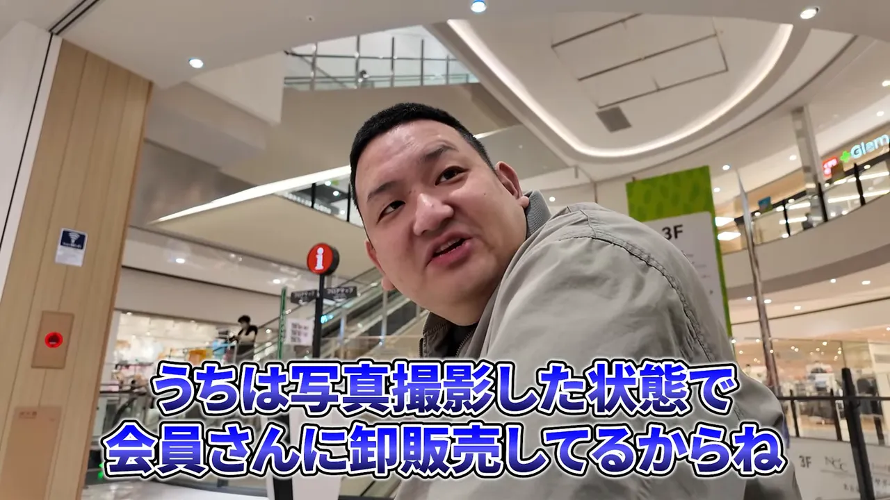 ショッピングモールの吹き抜けを背景に、検証結果と卸販売の説明をする男性のクリアな写真。