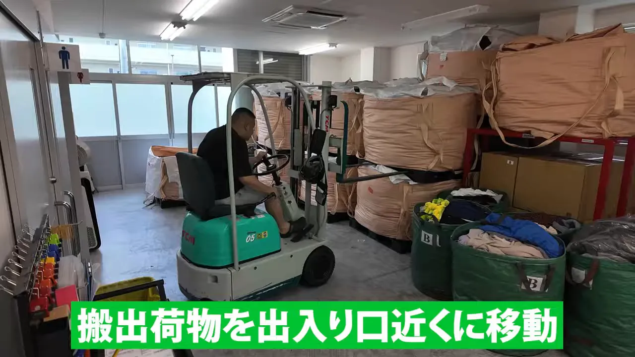 フォークリフトで茶色い大袋を倉庫の入口方向へ運んでいる