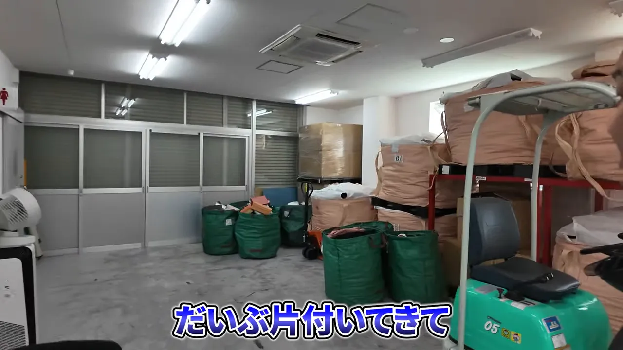 仕分け後の茶色い大袋と緑色の袋が倉庫の壁際にまとまり中央の床が空いている