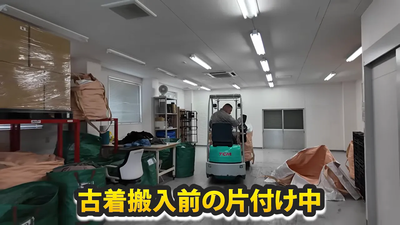倉庫内で搬入準備を進めるフォークリフトと古着の山