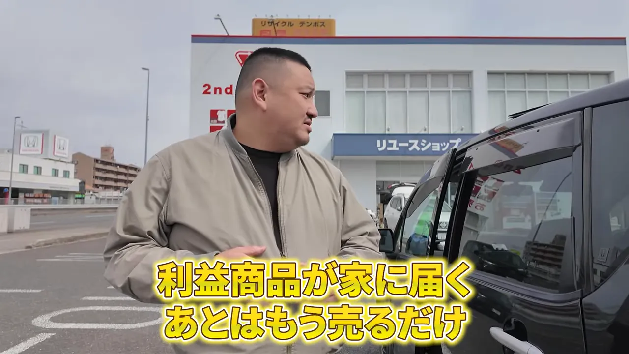 駐車場で話す男性に利益商品が家に届くという黄色テロップが表示された場面