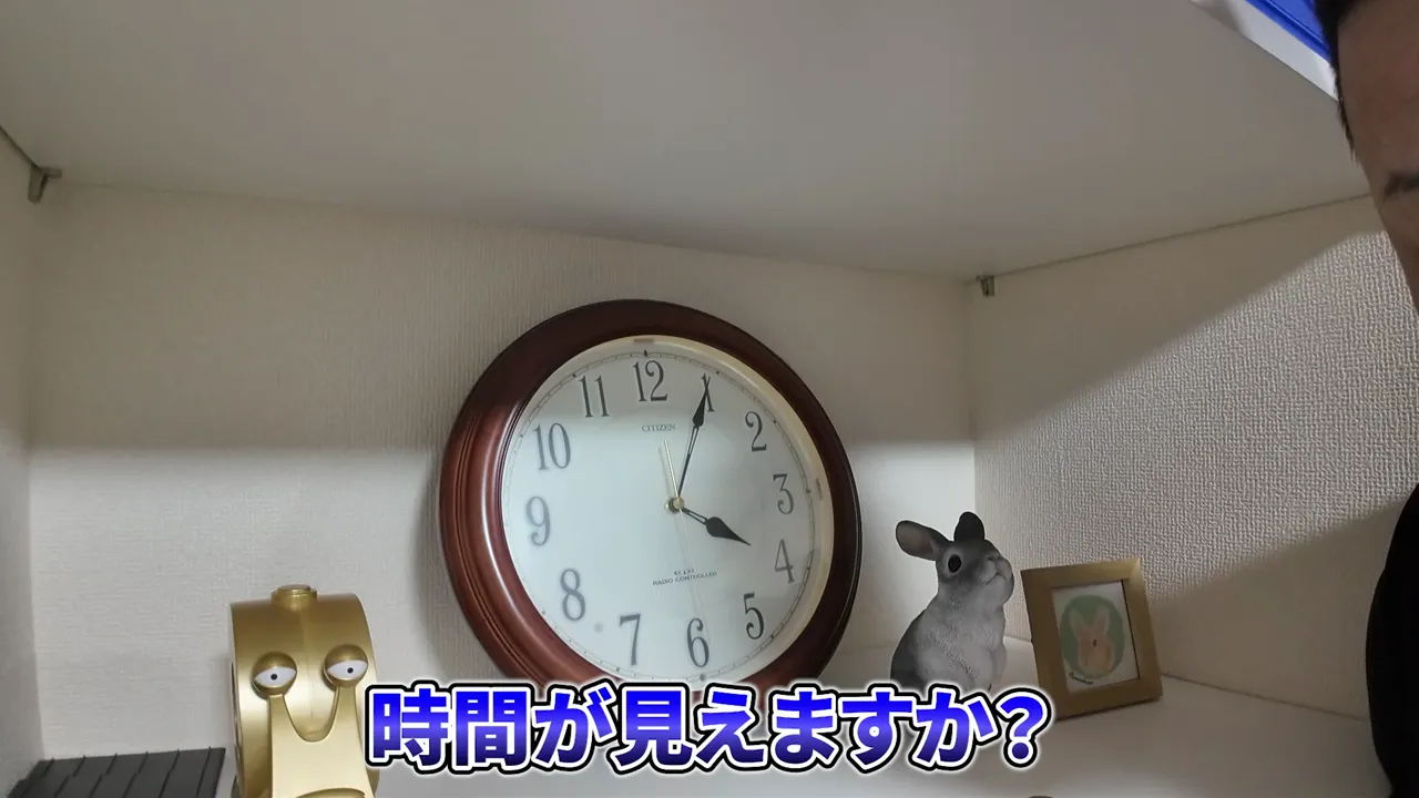 棚に置かれたアナログ時計と現在時刻4時05分の字幕