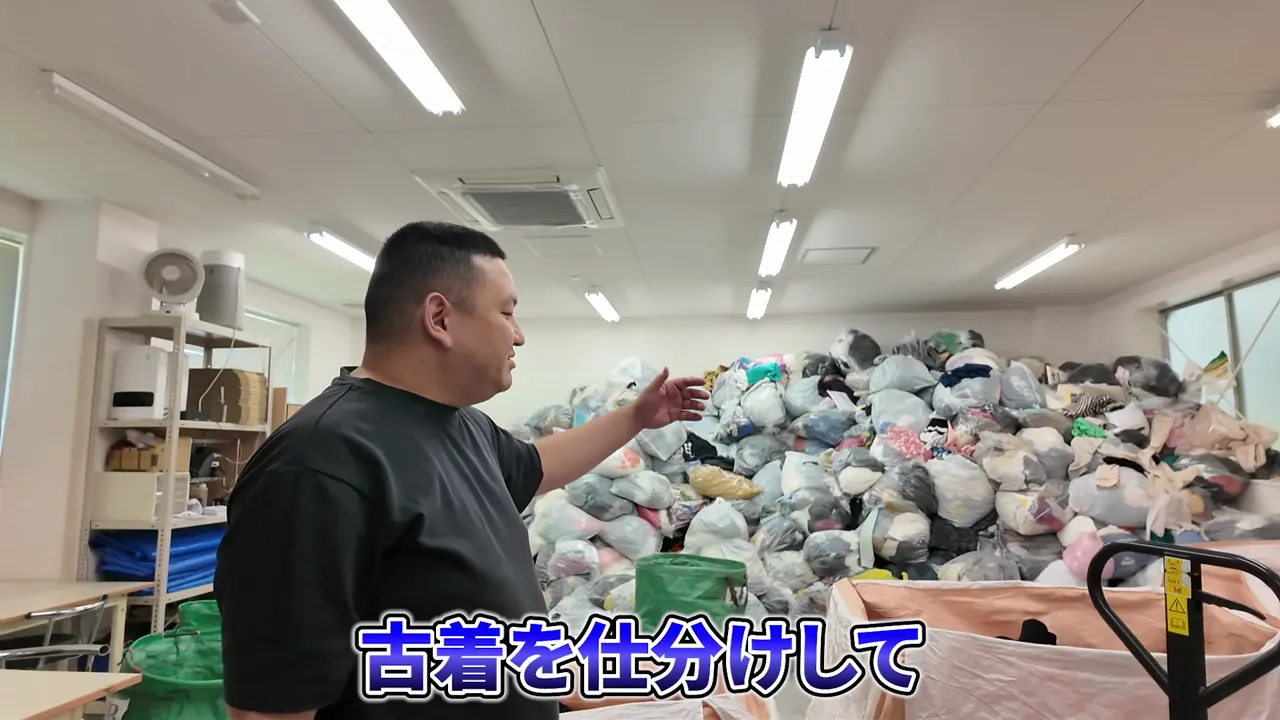倉庫に積まれた古着の袋を指し示す男性
