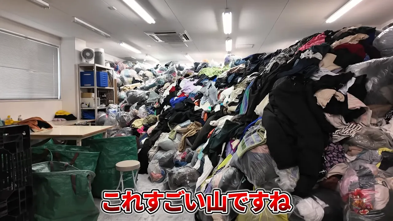 作業テーブルそばに積まれた大きな古着の山（クローズアップで明瞭）