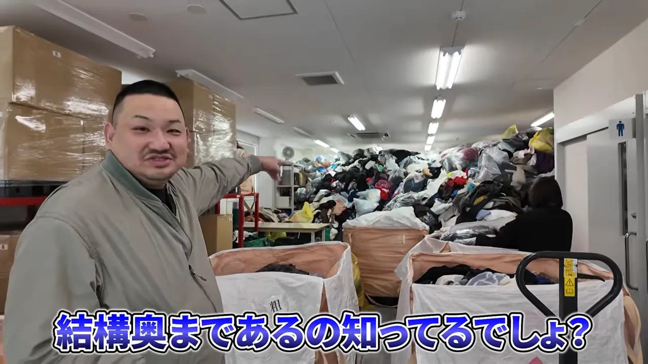 古着倉庫で大量の衣類を前に説明する作業者