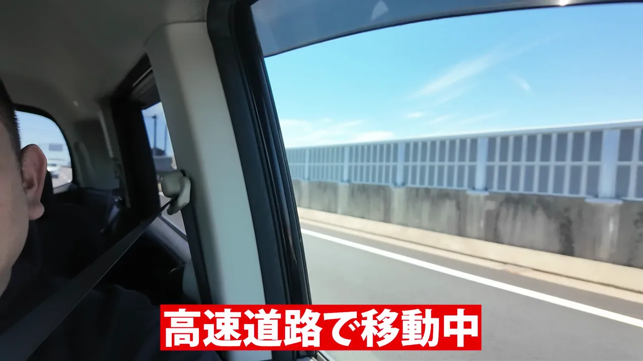 車窓から見える高速道路の防音壁と、高速道路で移動中という字幕