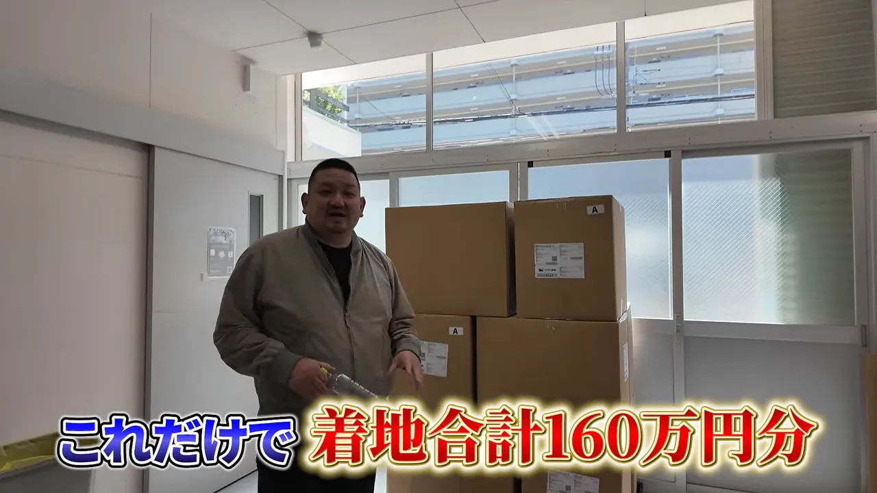 積み上がった箱の前で着地合計160万円分と説明している様子