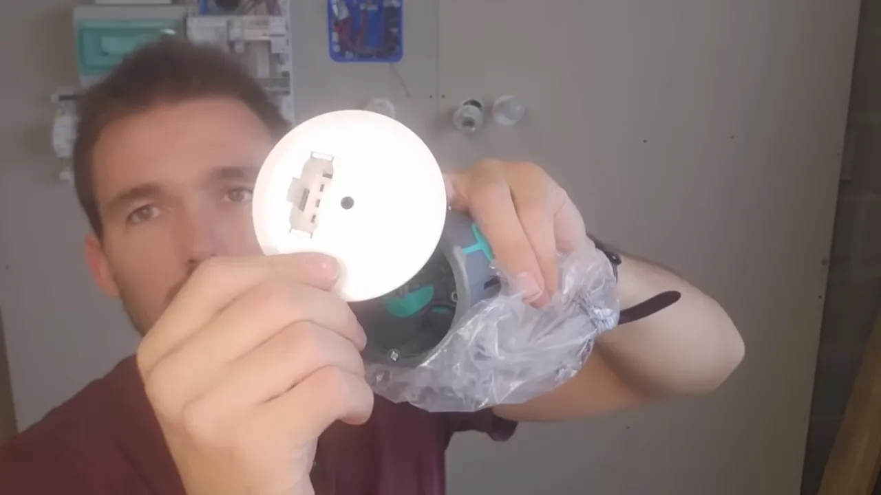 Gros plan montrant la platine blanche d'un boîtier d'encastrement (DCL) tenue devant la caméra, connexion visible.