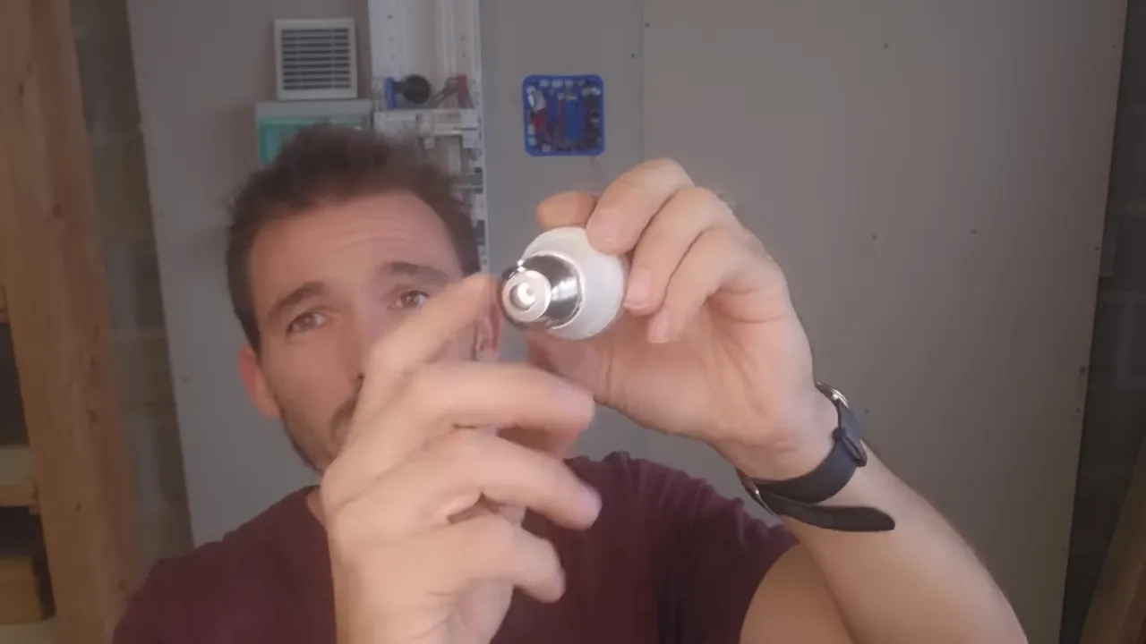 Gros plan sur le culot d'une ampoule tenu entre les mains, un doigt pointe le contact central.