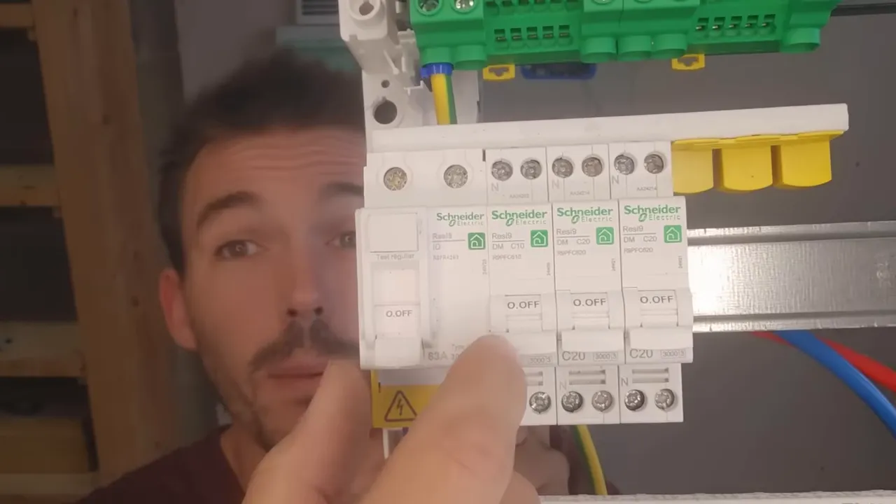 Gros plan sur des modules électriques (interrupteurs différentiels / disjoncteurs) dans un tableau, un doigt montre un module.