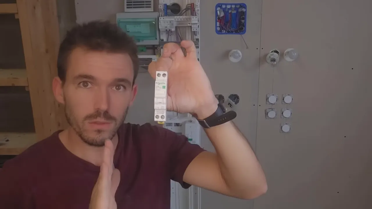 Présentateur tenant un disjoncteur Schneider C16 devant un tableau d'entraînement, vue nette