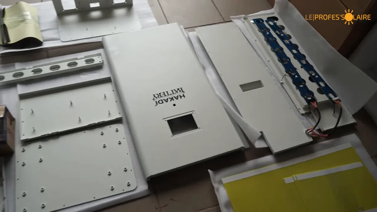 Pièces du kit batterie étalées au sol avec tôles, cartons, plaques isolantes et cartes PCB