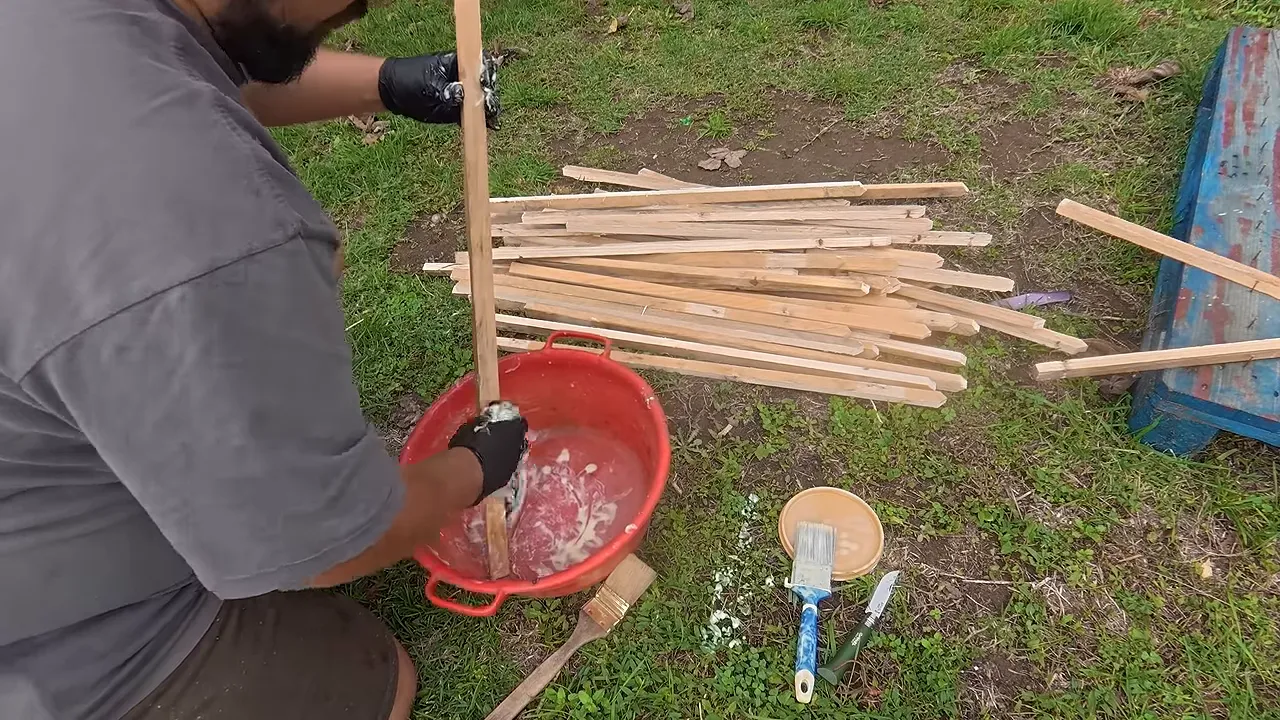 Application au chiffon sur une latte de bois au-dessus d’une bassine rouge, avec des gants noirs