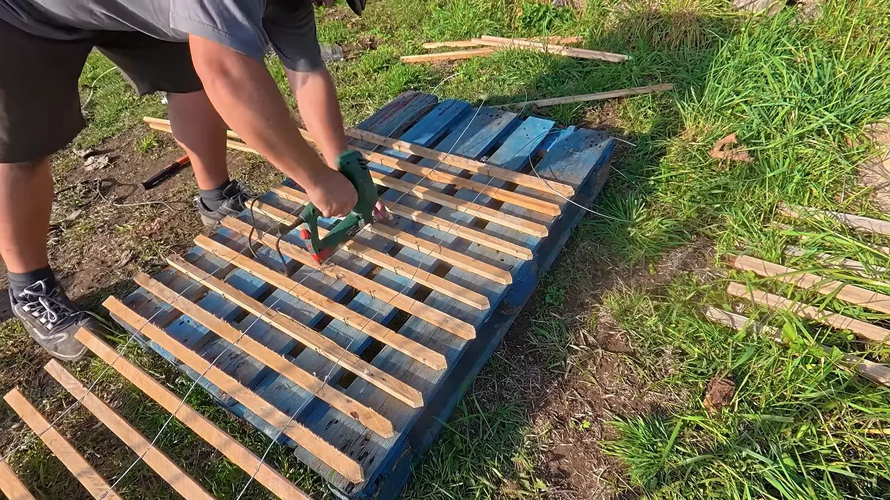Fixation à l’agrafeuse de lattes alignées sur une palette bleue