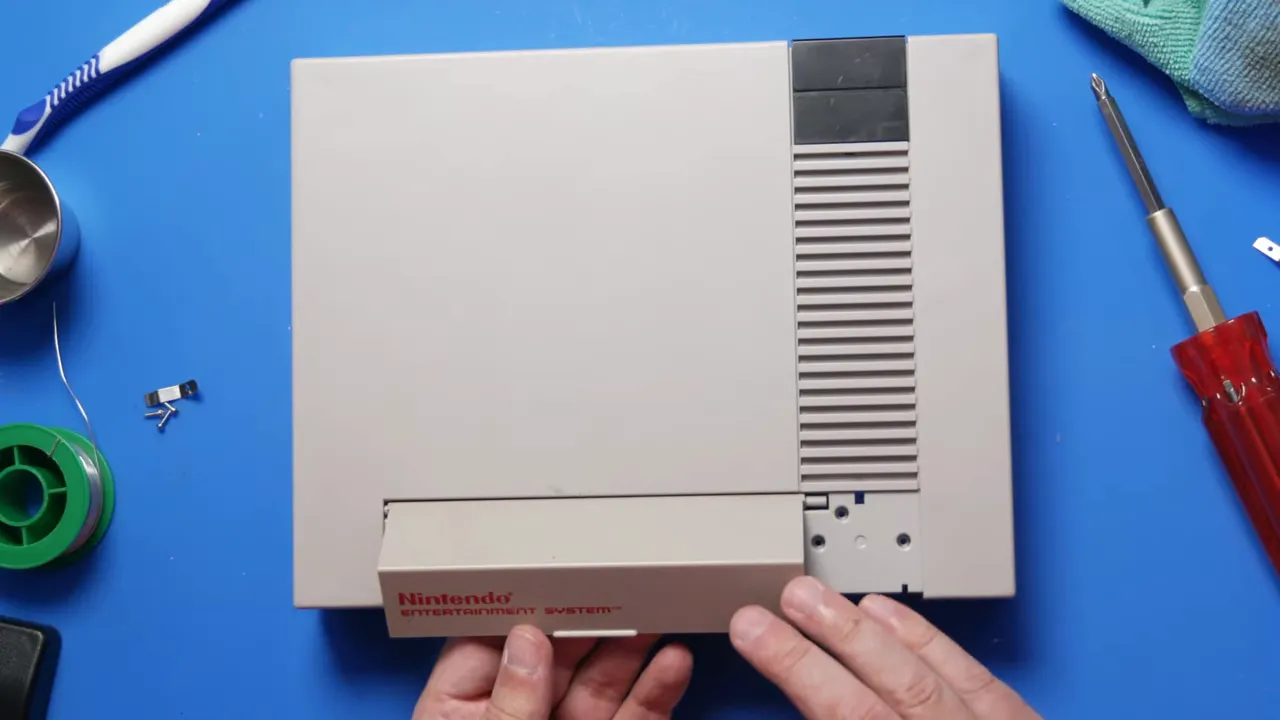 Coque supérieure de NES avec la porte avant installée et les mains sur le mécanisme