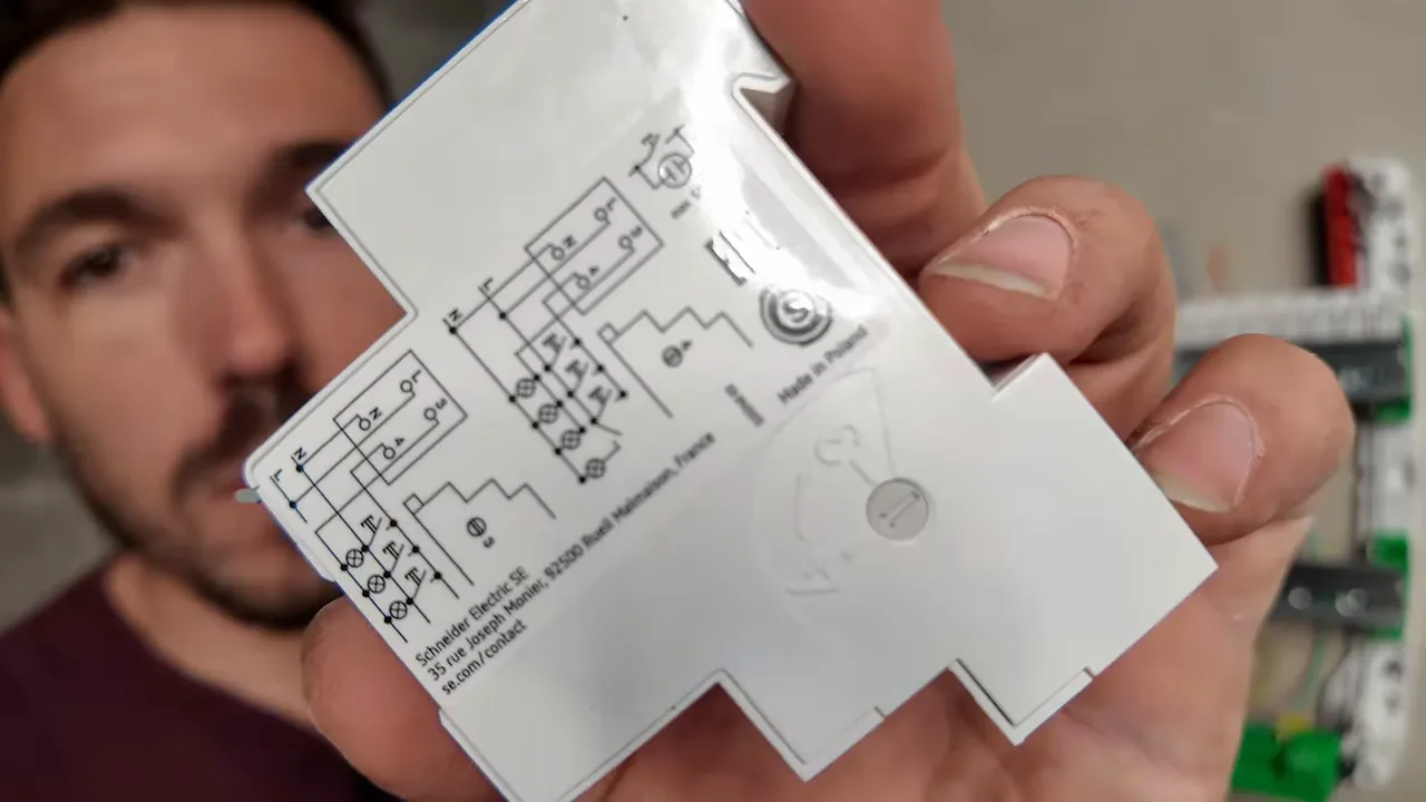 Minuterie modulaire tenue devant un tableau électrique avec repérage de ses bornes