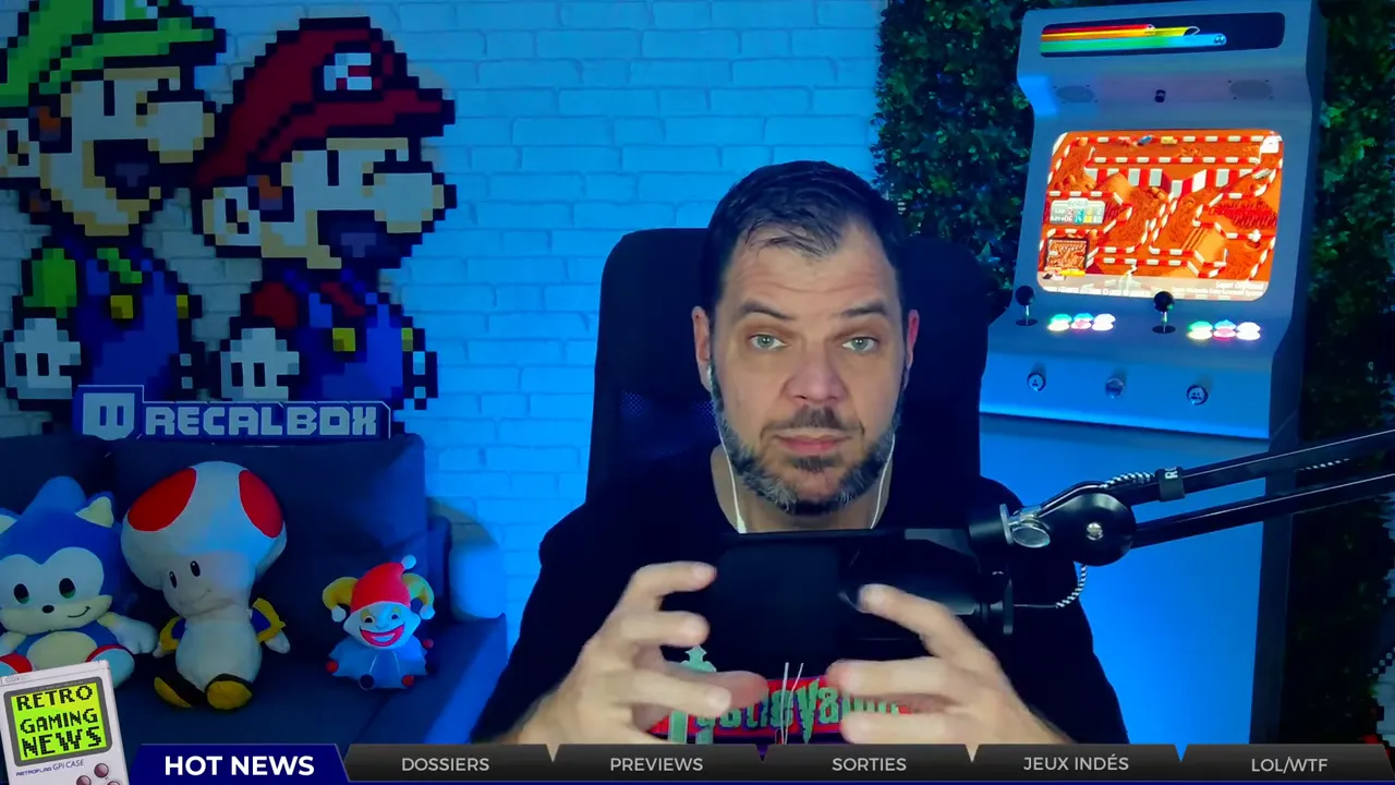 Animateur tenant une console portable devant la caméra, avec une borne d'arcade et décor rétro en arrière-plan