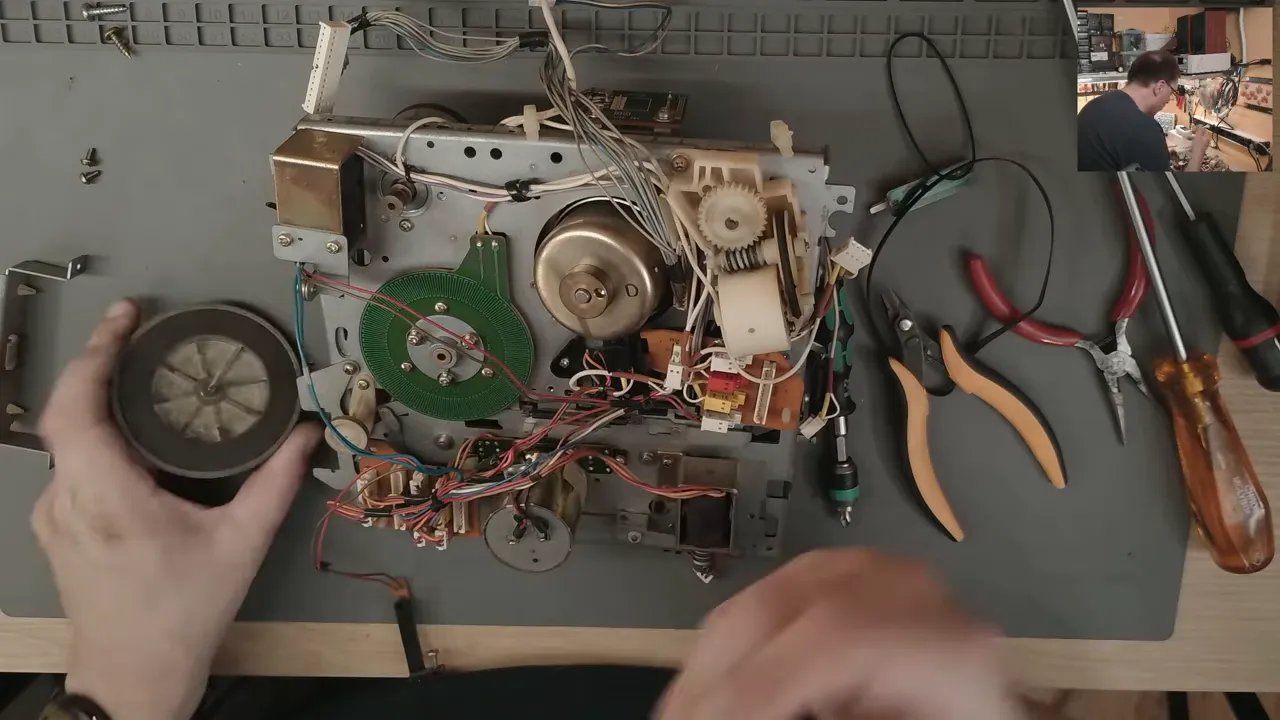 Mécanique VHS démontée avec poulies courroies et outils sur l'établi