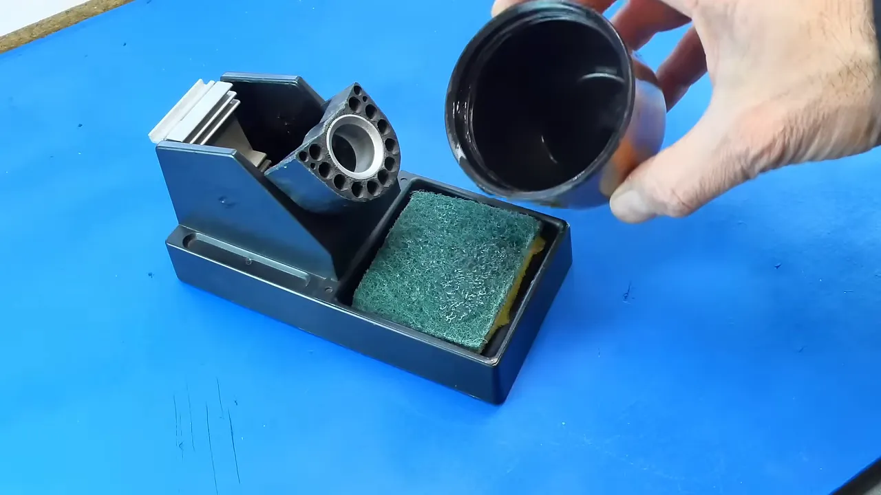 Support de fer à souder avec éponge humide dans le bac et main versant de l'eau depuis un récipient