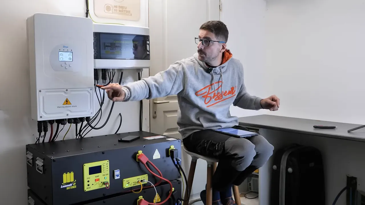 L’intervenant pointe l’onduleur et les câbles, illustrant les connexions de l’installation hybride