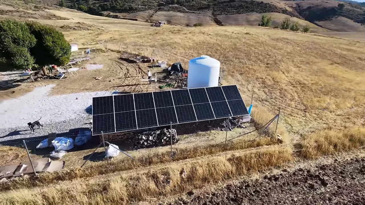 Rangée de panneaux solaires au sol devant une cuve blanche et la maison