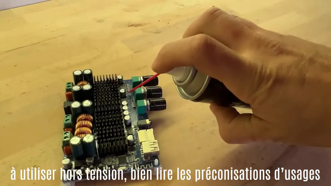 Main pulvérisant un nettoyant sur une carte électronique posée sur un établi