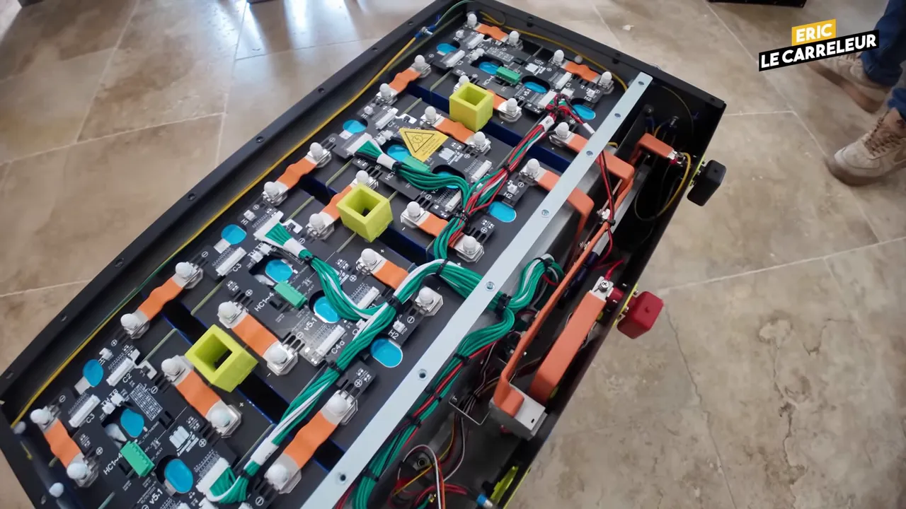 Vue rapprochée de l'intérieur d'une batterie domestique montrant les cellules, busbars orange et le câblage vert