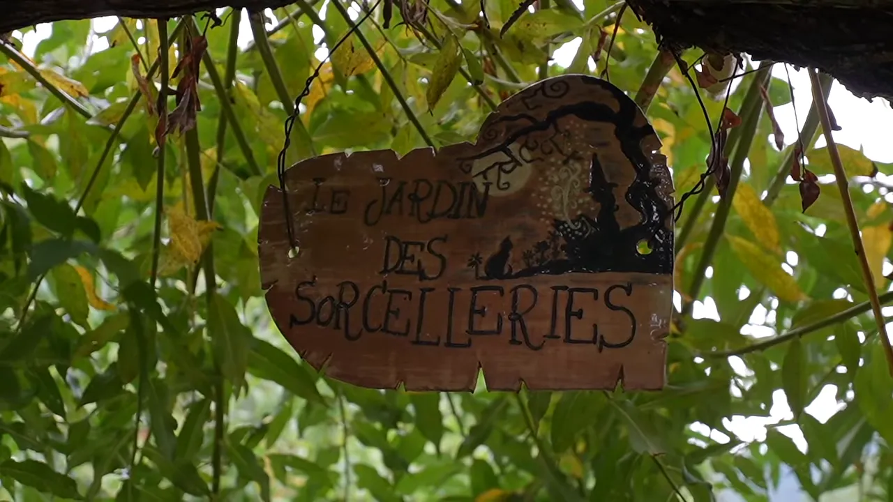Pancarte en bois marquée Le jardin des sorcelleries suspendue sous des feuilles