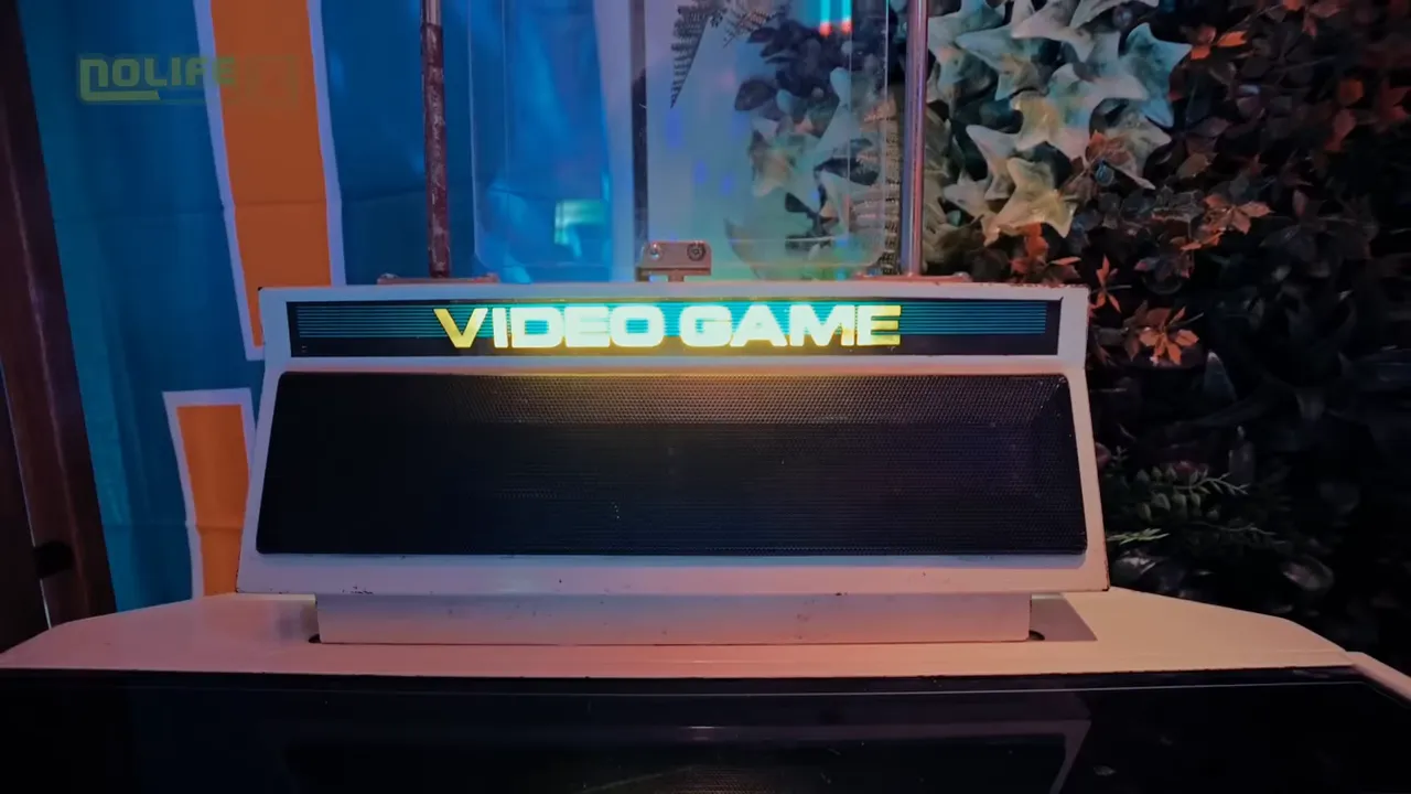 Marquise lumineuse « VIDEO GAME » d'une borne d'arcade, avec la grille haut-parleur et décor végétal derrière.