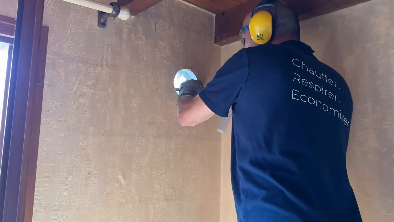Installateur en train de réaliser une intervention sur un mur intérieur lors de la pose du système aérothermique