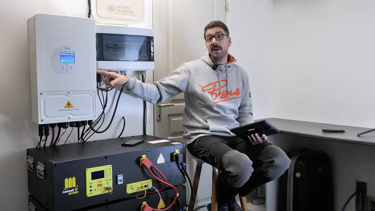 Intervenant pointant vers l'onduleur et le coffret électrique avec câbles et batteries en avant-plan