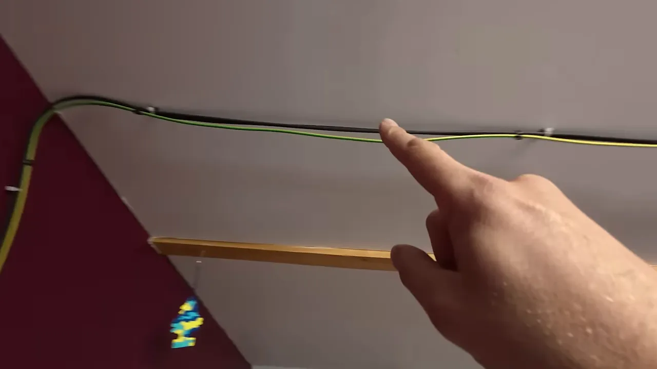 Câbles solaires (noir et vert/jaune) fixés au plafond avec colliers, doigt montrant le chemin